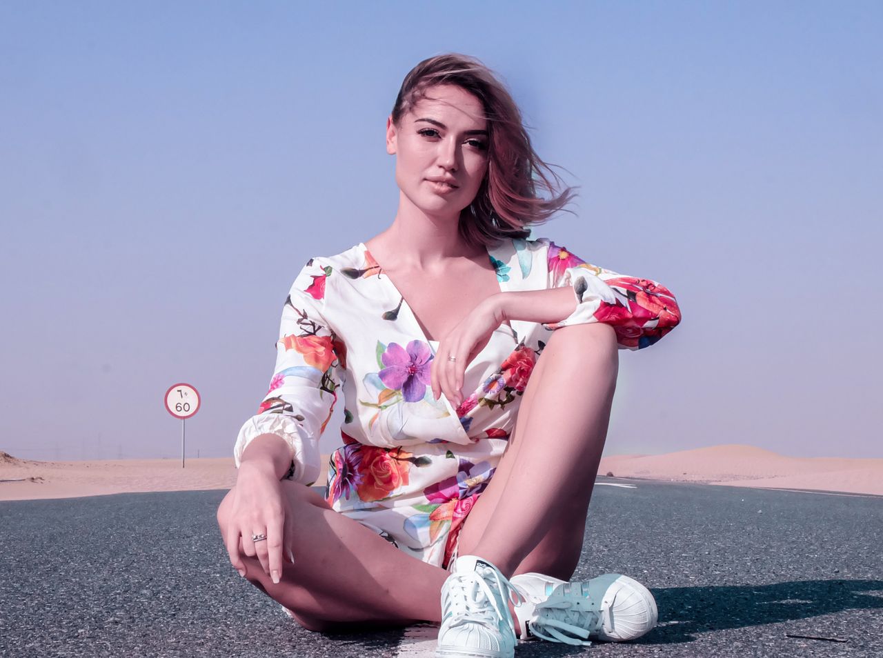 Elegant woman in floral dress sitting on road in Dubai desert, enjoying a sunny day.